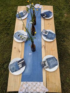 a long table with plates and vases on it in the middle of some grass