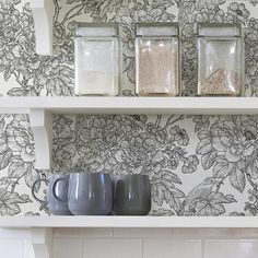 some jars and cups are sitting on a shelf in front of a wallpapered wall