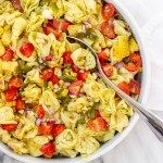 a white bowl filled with pasta salad on top of a marble counter next to a fork