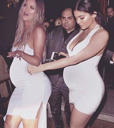 two women in white dresses are dancing at a party with other people behind them and one woman is holding her phone