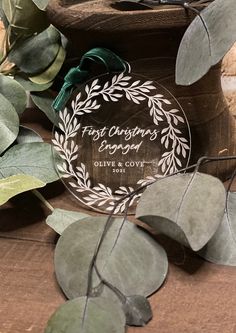 the first christmas ornament is surrounded by eucalyptus leaves and other greenery on a wooden surface