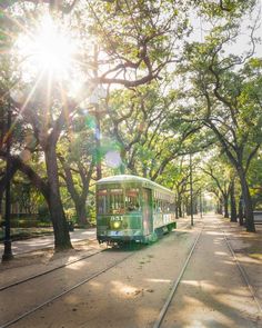 a green trolley car traveling down a tree lined street