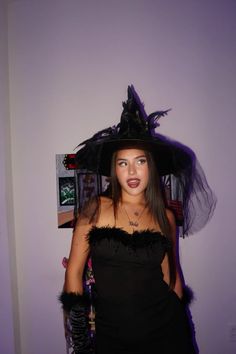 a woman in a black dress and hat with feathers on her head posing for the camera