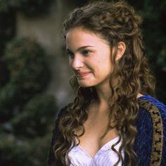 a woman with long curly hair wearing a blue and white dress smiling at the camera