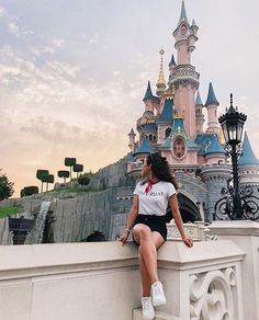 a woman sitting on top of a stone wall next to a castle with a waterfall