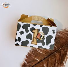 a brown and white cow print bag with a number one on the front, sitting next to a feather