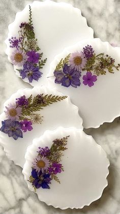 three plates with purple flowers on them sitting on a marble counter top next to each other