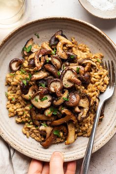 someone is holding a fork over a plate of rice with mushrooms and parsley on the side