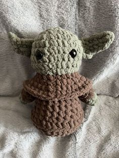 a crocheted baby yoda doll sitting on top of a white bed sheet