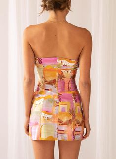 the back of a woman wearing a short dress with an orange and pink print on it