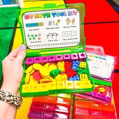 a child's hand is holding an open plastic box filled with different colored toys