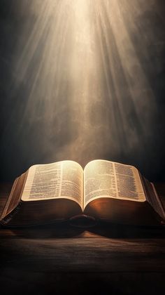 an open book sitting on top of a wooden table under a beam of sunbeams