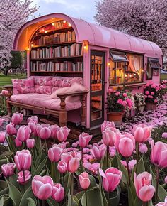 a pink couch sitting in front of a book shelf filled with books next to flowers