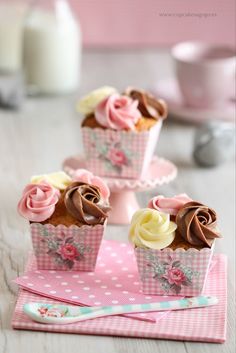 three cupcakes with chocolate frosting and pink flowers on them sitting on a table