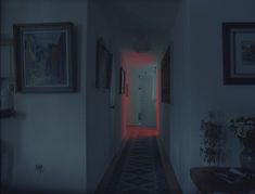 an empty hallway with red light coming from the door and framed pictures on the wall