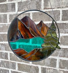 a circular stained glass window hanging on a brick wall with mountains and trees in the background