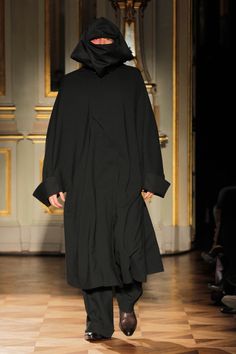 a man in a black coat walking down a runway