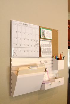 a bulletin board mounted to the side of a wall with calendars and pens on it