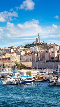 several boats are docked in the water near a city on a hill behind them,