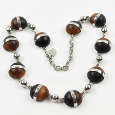 This is part of Chairish’s Costume Jewelry assortment.  Elegant modernist Balenciaga Paris signed necklace. It features a choker shape with a chromed metal chain ornate with geometric half-sphere cabochons in exotic woods. Signed with chrome metal tag at clasp: "BB - Balenciaga - Made in France". Spring-ring closing clasp with adjustable chain for length flexibility.  Measurements: necklace's total length is 19.69 in long (50 cm) - each cabochon element is 0.82 in diameter (2 cm).  Please see th Modern Round Cabochon Necklace, Modern Cabochon Necklace, Elegant Brown Necklace With Polished Finish, Modernist Metal Necklace With Polished Finish, Elegant Necklaces With Wooden Beads, Elegant Wooden Beads Necklace, France Spring, Balenciaga Jewelry, Metal Tag