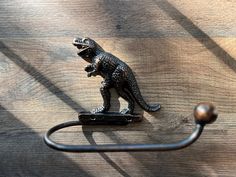 a metal towel hook with a small toy dinosaur on it's side, sitting on top of a wooden surface