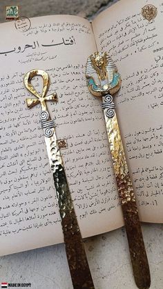 an open book with two gold and silver scissors on it next to each other in arabic writing