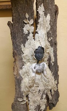 a small statue sitting on top of a piece of wood next to a tree trunk