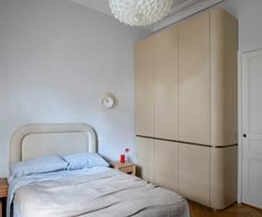 a white bed sitting next to a wooden dresser under a light hanging from a ceiling fan