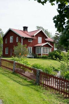 a red house with white windows and a wooden fence in front of it on a green lawn