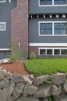 an apartment building with grass and rocks in the foreground, next to a stone wall