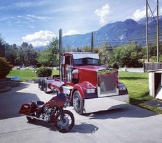 a red semi truck parked next to a motorcycle in a parking lot with mountains in the background