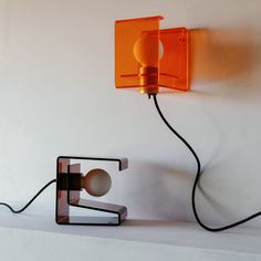 an orange lamp sitting on top of a table next to a wall mounted light fixture