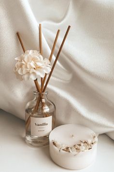 a vase filled with flowers next to a white container on top of a bed covered in sheets