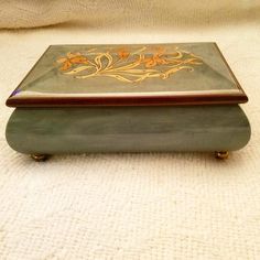 a green and gold box sitting on top of a white blanket covered floor next to a wall