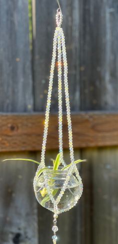 a glass hanging planter with beaded strings and flowers in it's center