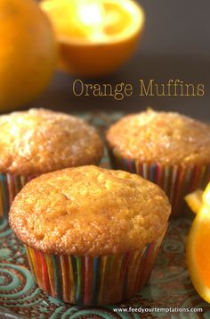 three orange muffins sitting on top of a plate next to an orange slice