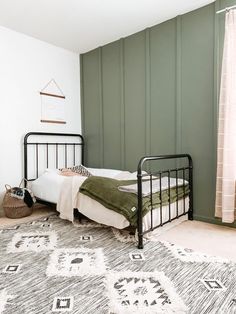 a black metal bed frame in a green room with rugs and pillows on the floor