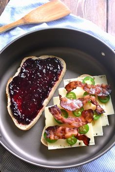 two pieces of bread with jam and bacon on them in a pan next to a spoon