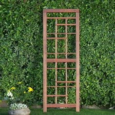 a wooden trellis sitting in front of a green hedge