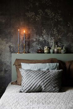 a bed with two candles on the headboard and pillows in front of it,