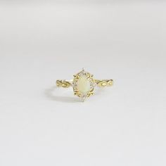 a yellow gold ring with an oval opal and diamond accenting the band, on a white background