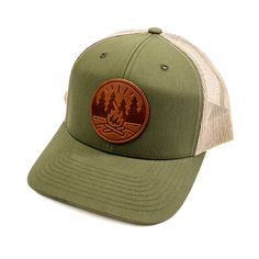 Get Fired Up for Adventure with this Campfire Cap! The patch on this hat features a classic campfire scene, capturing the timeless allure of the great outdoors. It's a simple yet evocative image: two logs ablaze with flames reaching upwards, cradled by a circle that hints at the unity and completeness of nature. The trees standing sentinel on either side anchor the scene in the wild, calling to mind the serenity of the woods and the simple pleasures of a fireside chat under the stars. Each cap i Campfire Scene, Vintage Baseball Caps, Leather Stand, Pocket Notebook, Getting Fired, A Circle, Under The Stars, Mesh Panel, Simple Pleasures