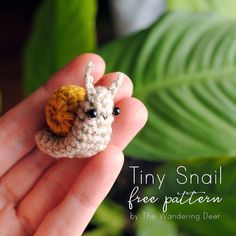 tiny small crocheted animal sitting on top of someone's hand with the caption tiny snail free pattern by the wandering deer