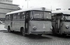 two old buses parked next to each other on a brick road with buildings in the background