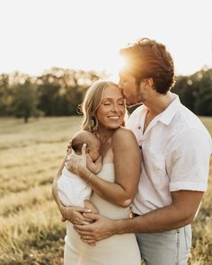 a man and woman holding a baby in a field at sunset with the sun shining on them