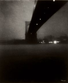 black and white photograph of the brooklyn bridge at night, taken from across the river