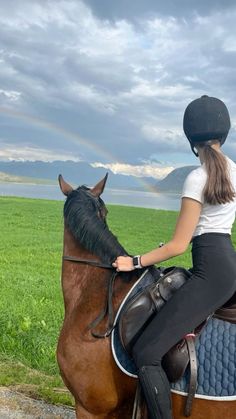 a woman riding on the back of a brown horse next to a lush green field