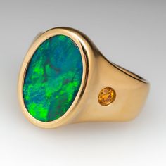 The satin finished ring is centered with a bezel set, oval, black opal cabochon. The shoulders are each flush set with one (1) round brilliant cut, fancy intense orange-yellow diamond. The ring measures 19.2mm at the top, rises 6.1mm above the finger, tapering to 5.4mm wide and 1.5mm thick at the base of the shank. We offer complimentary ring sizing to fit. Oval Opal Ring With Bezel Setting For Formal Occasions, Modern Oval Opal Ring For Formal Occasions, Modern 14k Gold Oval Opal Ring, Modern Oval Yellow Gold Opal Ring, Modern Yellow Gold Oval Opal Ring, Modern Oval Opal Ring In Yellow Gold, Modern Gold Oval Opal Ring, Modern Oval Opal Ring, Luxury Oval Opal Ring With Bezel Setting