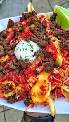 a white plate topped with tacos and fries next to a lime wedge on top of a table