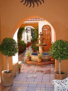 an image of a house with a fountain in the middle and potted plants on either side